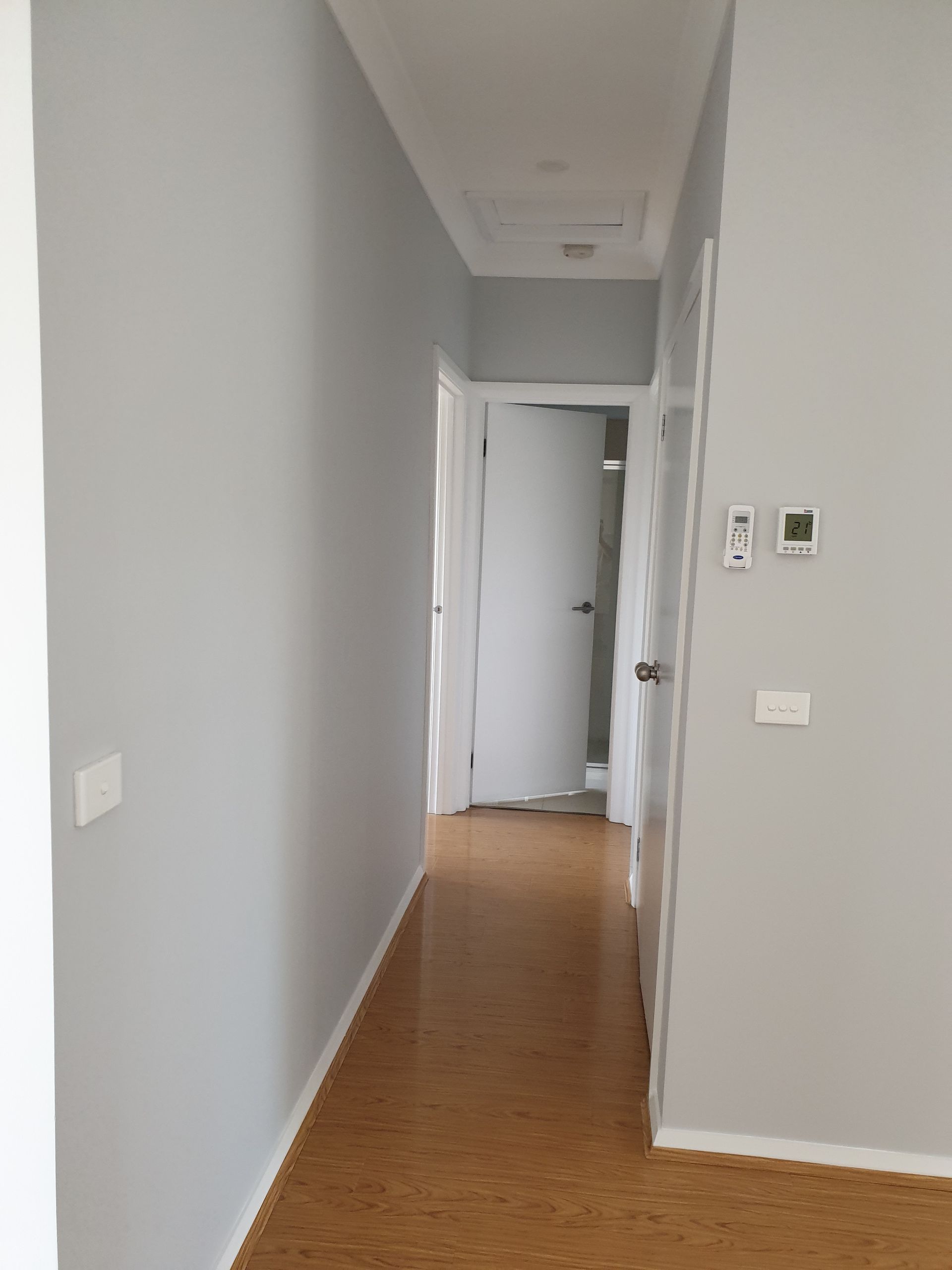 Narrow hallway with gray walls, wood floor, and white doors leading to an interior room.