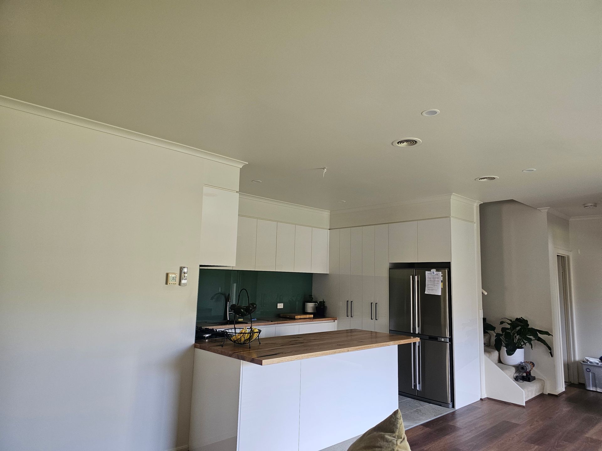 Bright white kitchen with stainless fridge, island counter, and dark green backsplash in an open room