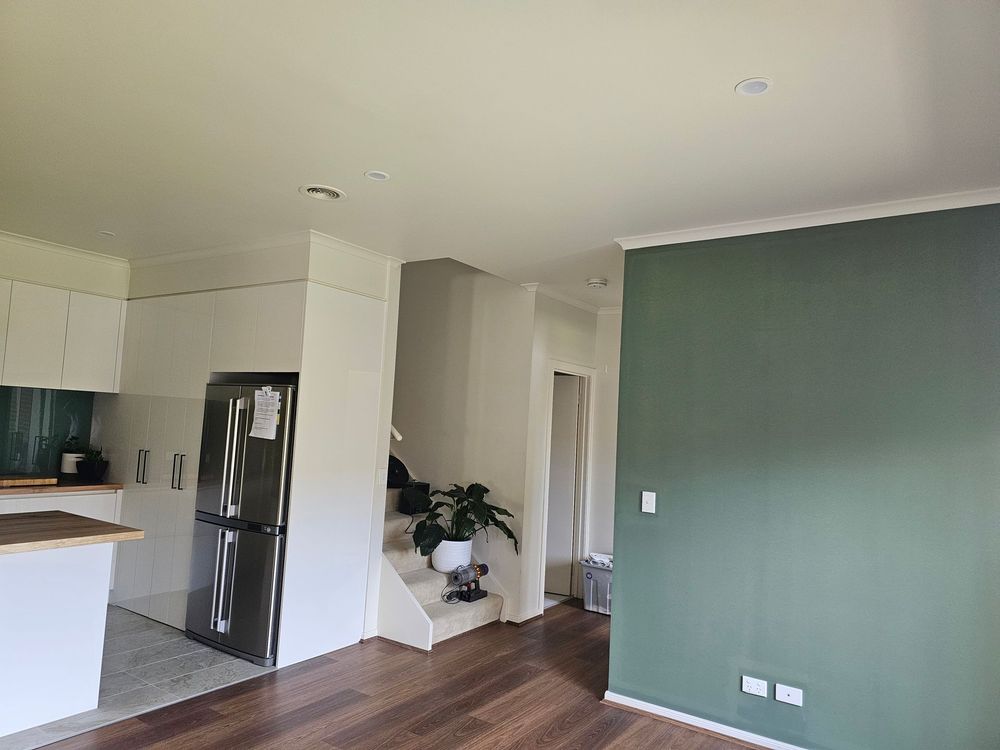 Modern kitchen and living area with white cabinets, black fridge, green accent wall, and potted plant by stairs