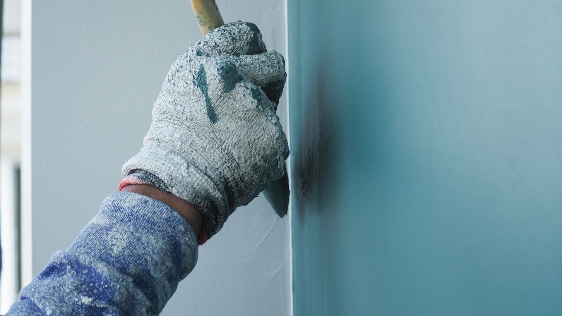 Gloved hand painting a light blue wall with a brush