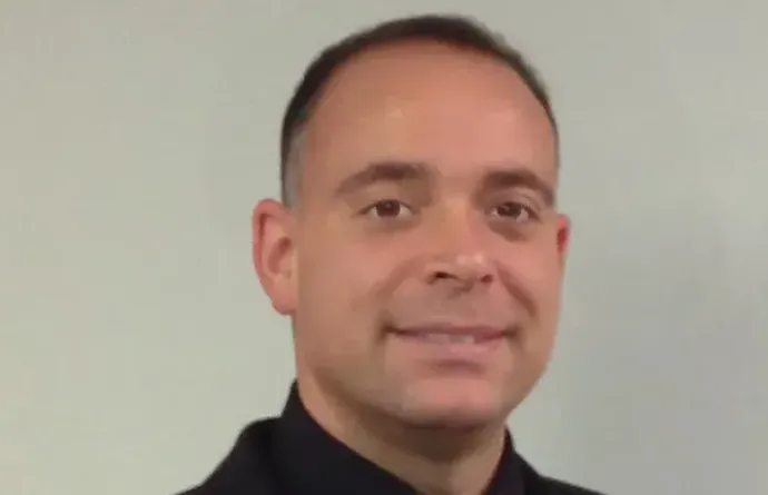 A man in a black shirt and tie is smiling for the camera.