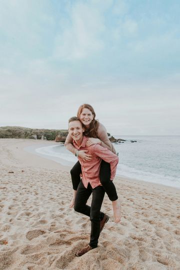 A man is carrying a woman on his back on the beach.