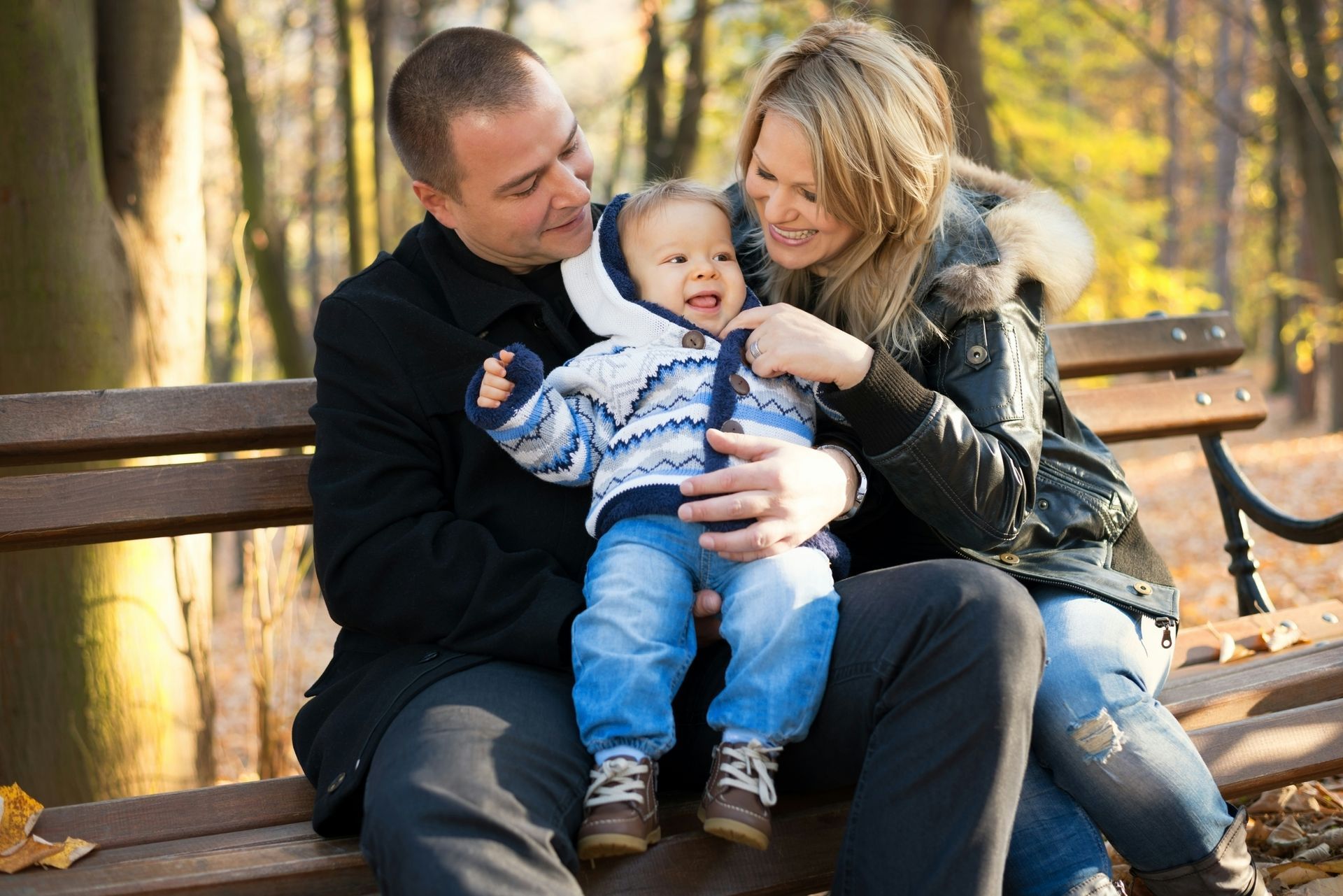 A man and woman are sitting on a park bench holding a baby.