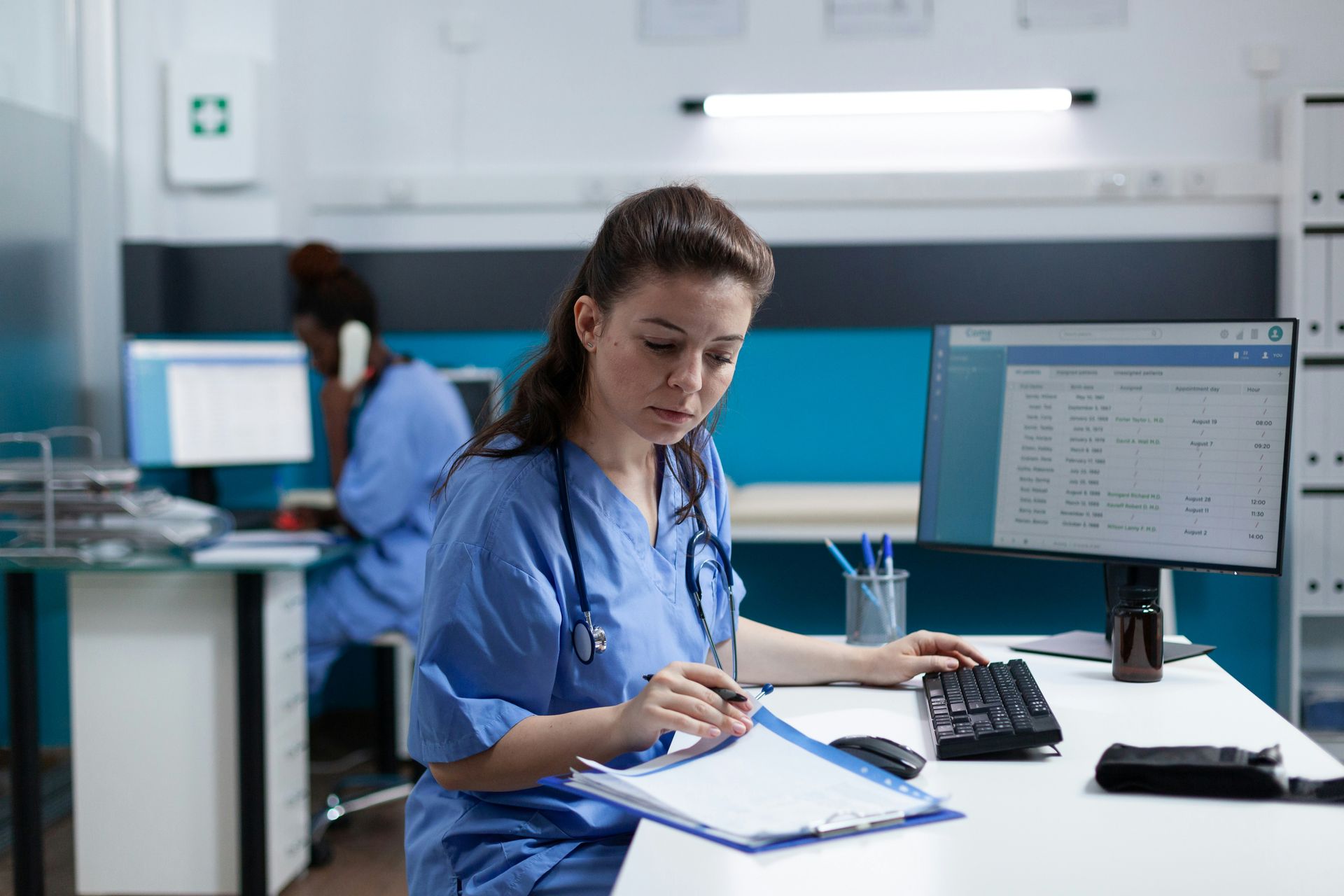 A nurse is sitting at a desk in front of a computer.