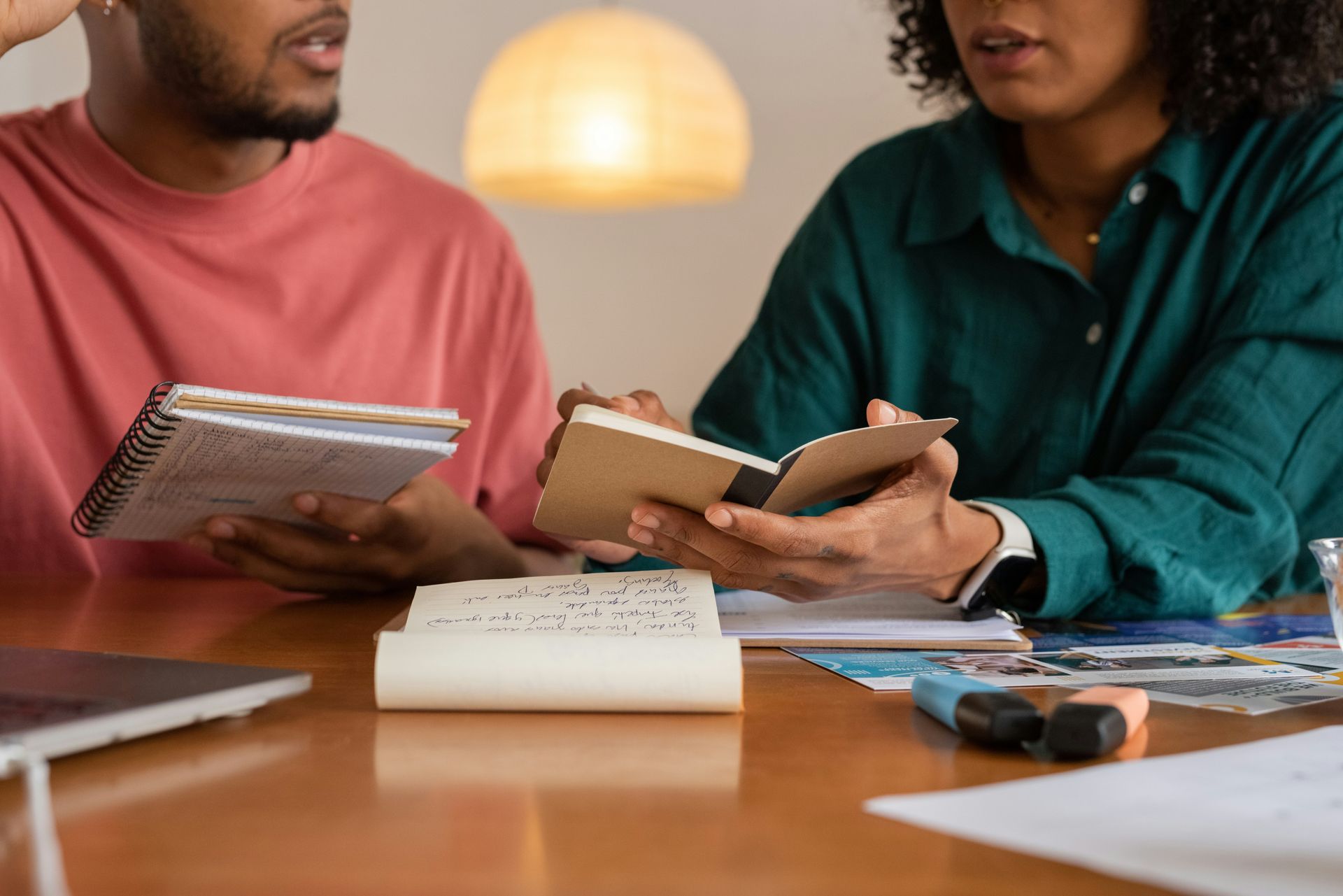 A man and a woman are sitting at a table holding notebooks.