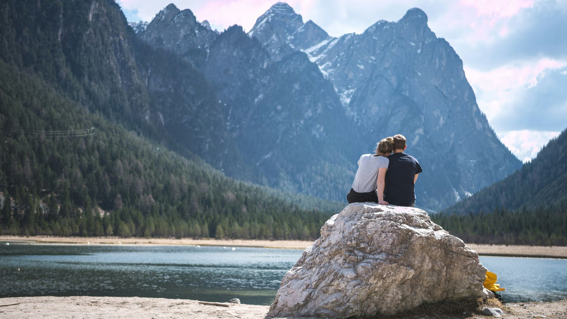 A man and a woman are sitting on a rock overlooking a lake.