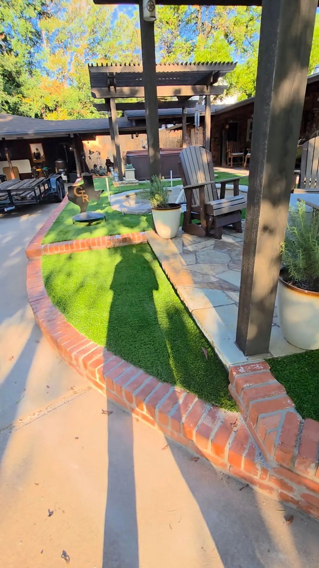 Sunny garden courtyard with green turf path, brick edging, trees, and outdoor seating near a building