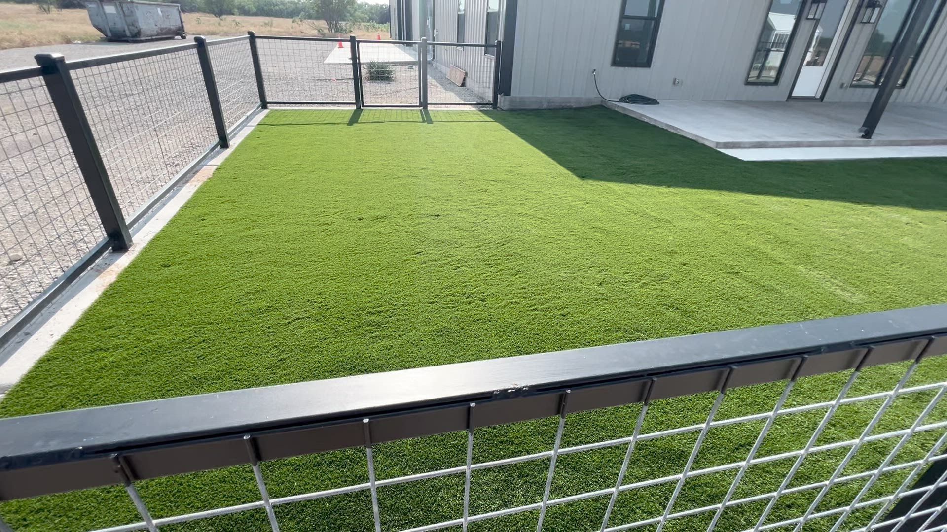 Freshly installed green turf in a fenced backyard beside a house and patio.