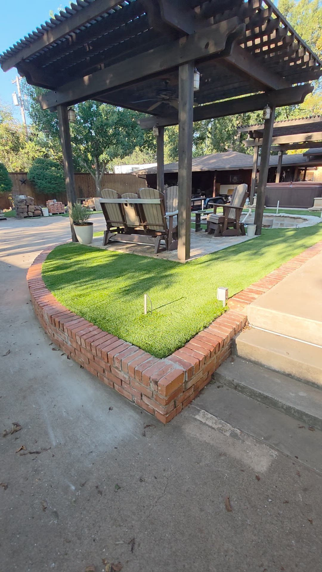 Covered outdoor seating area with tables and chairs on a grassy patio beside a paved walkway