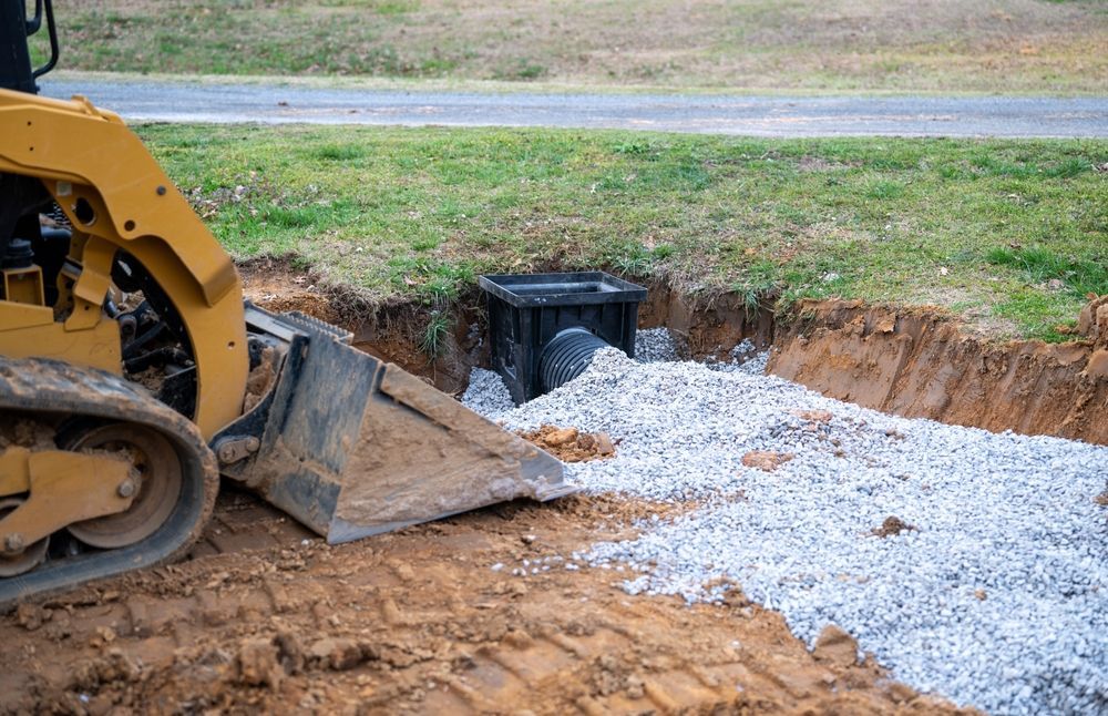 Bulldozer spreading gravel in a dug-out trench around a drainage pipe at a construction site