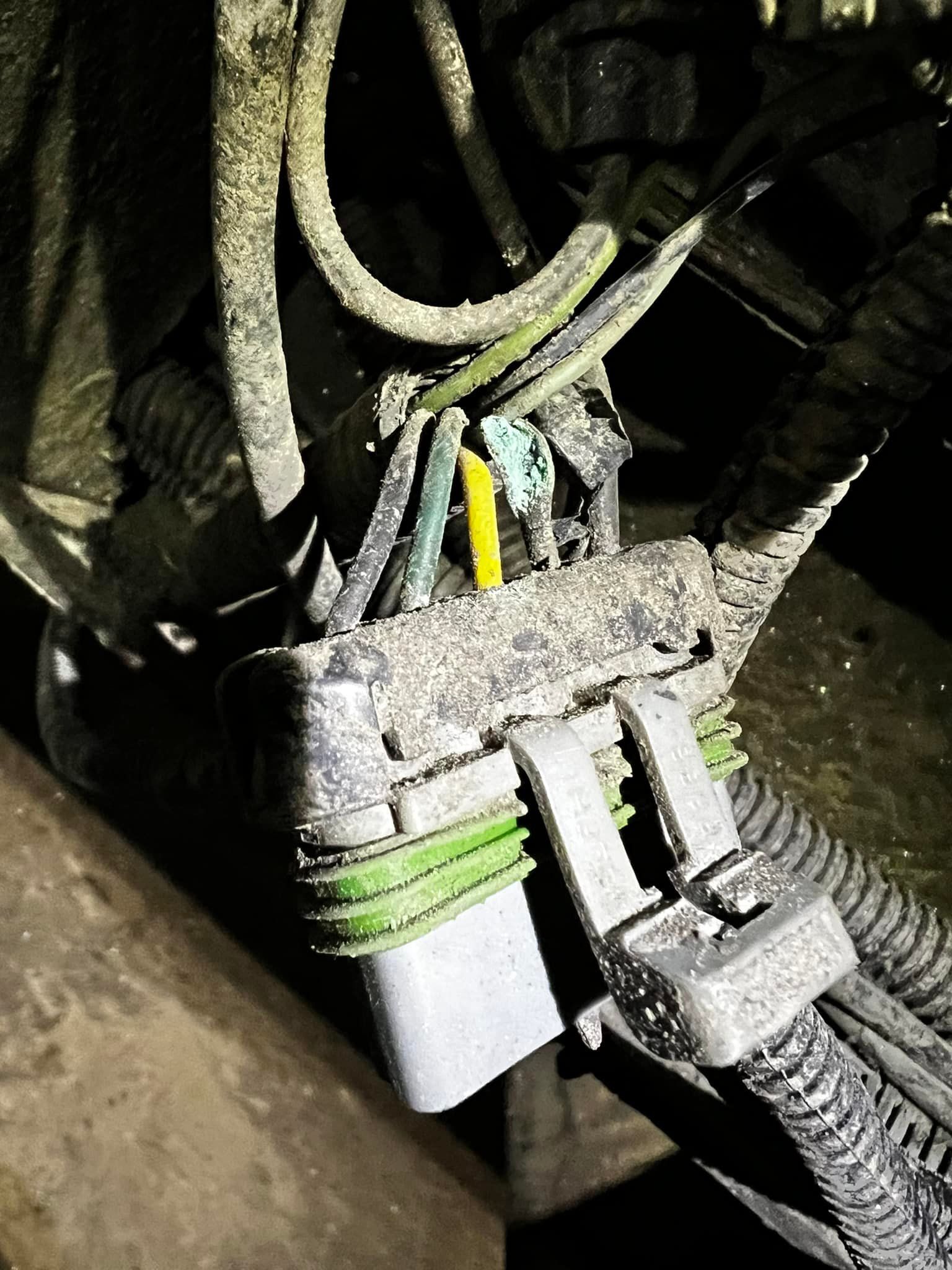 Close-up of a dusty car electrical connector with wires of different colors: yellow, green, and black.