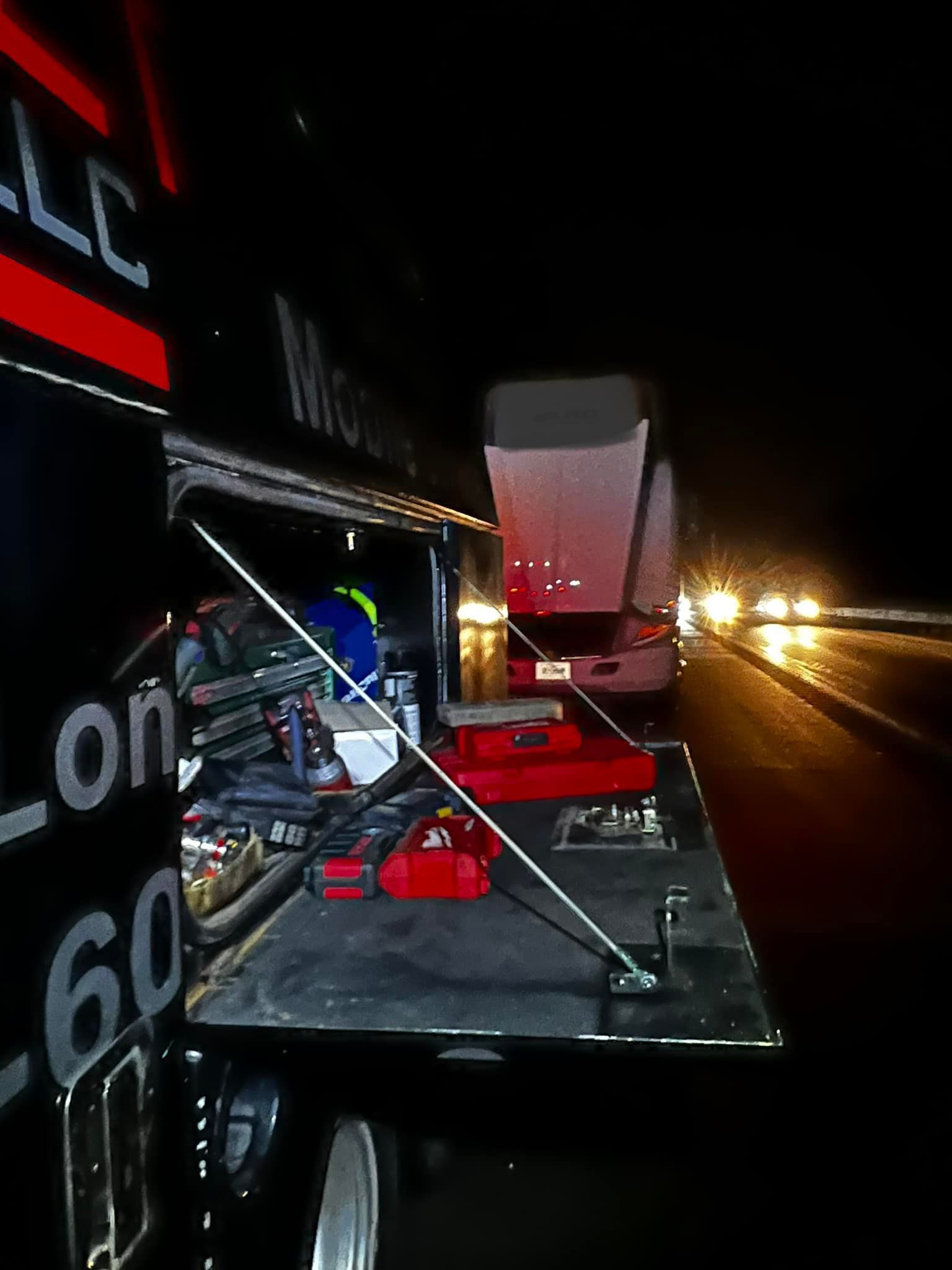 Open tool compartment of a black truck at night, with tools and a car visible.