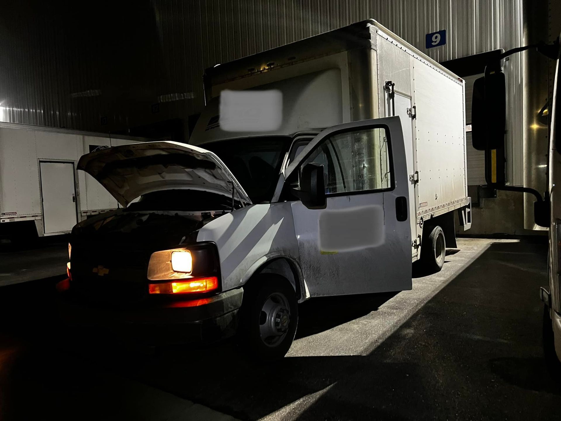 White box truck with hood and door open, parked at night.