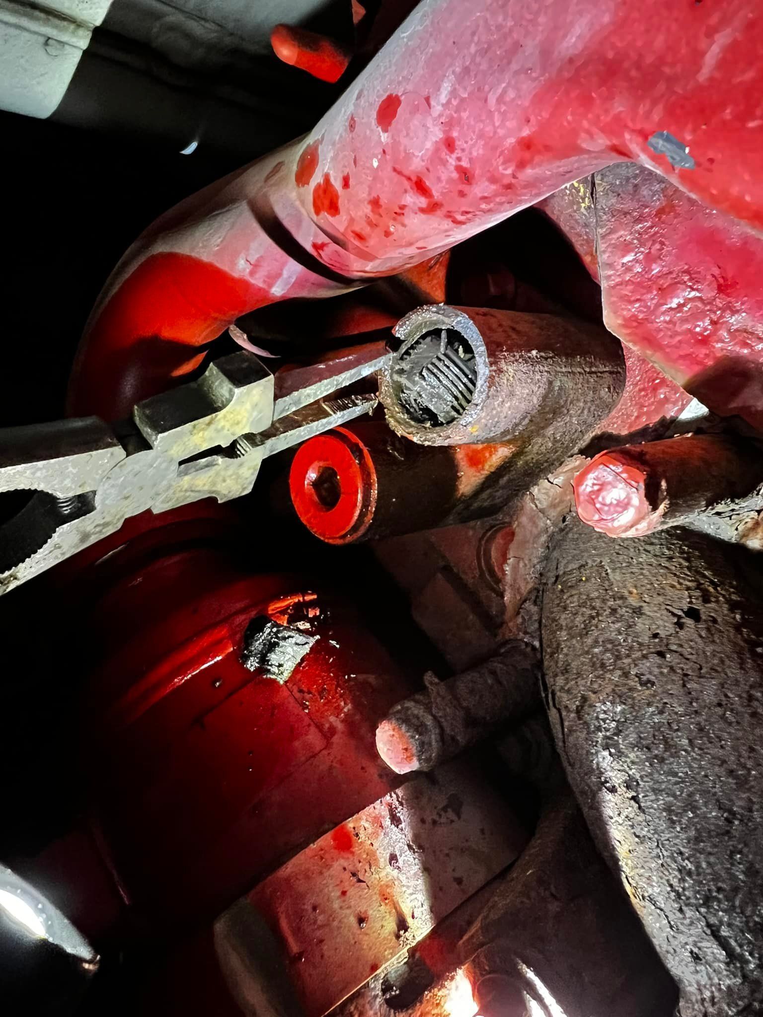 Pliers grip a metal clip within a red automotive component, likely for repair.