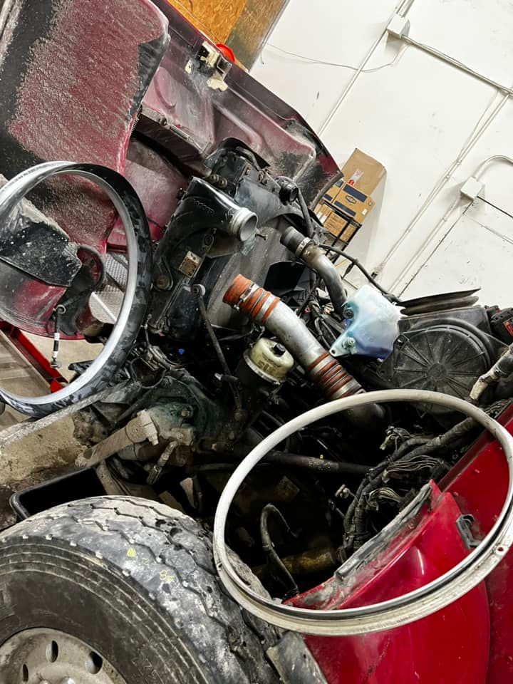 Wrecked red vehicle engine components; twisted metal and tires dominate the scene within a garage setting.