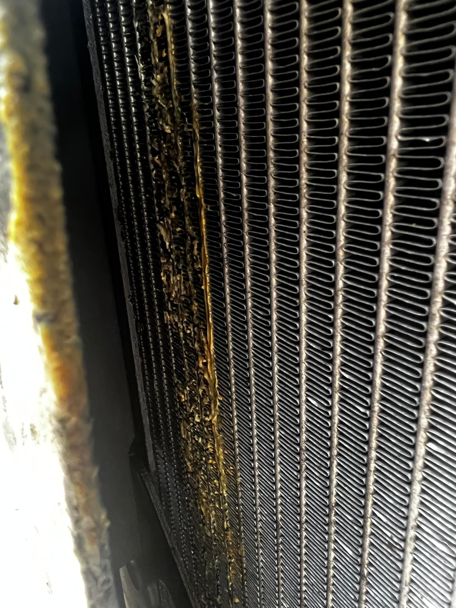 Close-up view of a vehicle radiator with oily, yellow-brown residue along the fins.