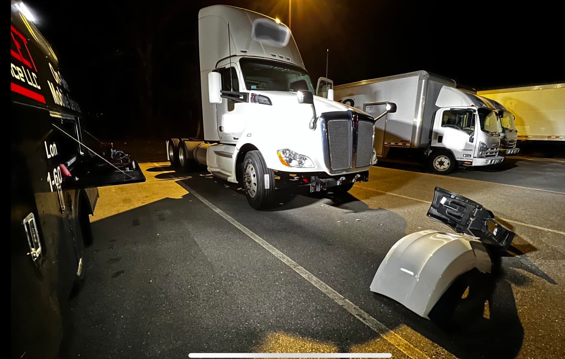 White semi-truck parked at night, fender detached on pavement.