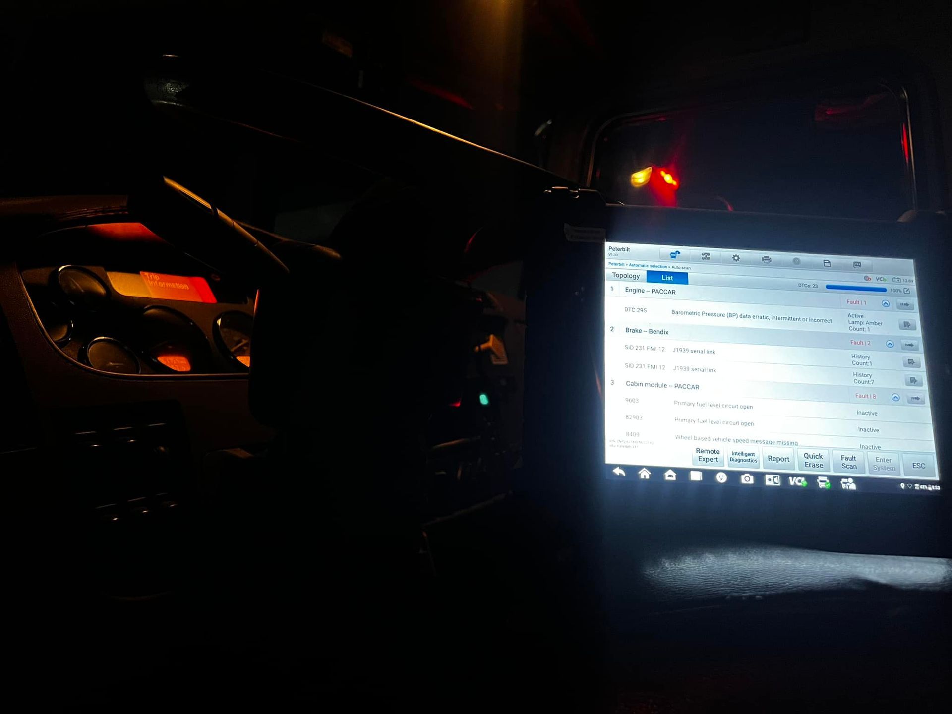 A diagnostic tablet inside a dark vehicle. The screen is lit, displaying data.