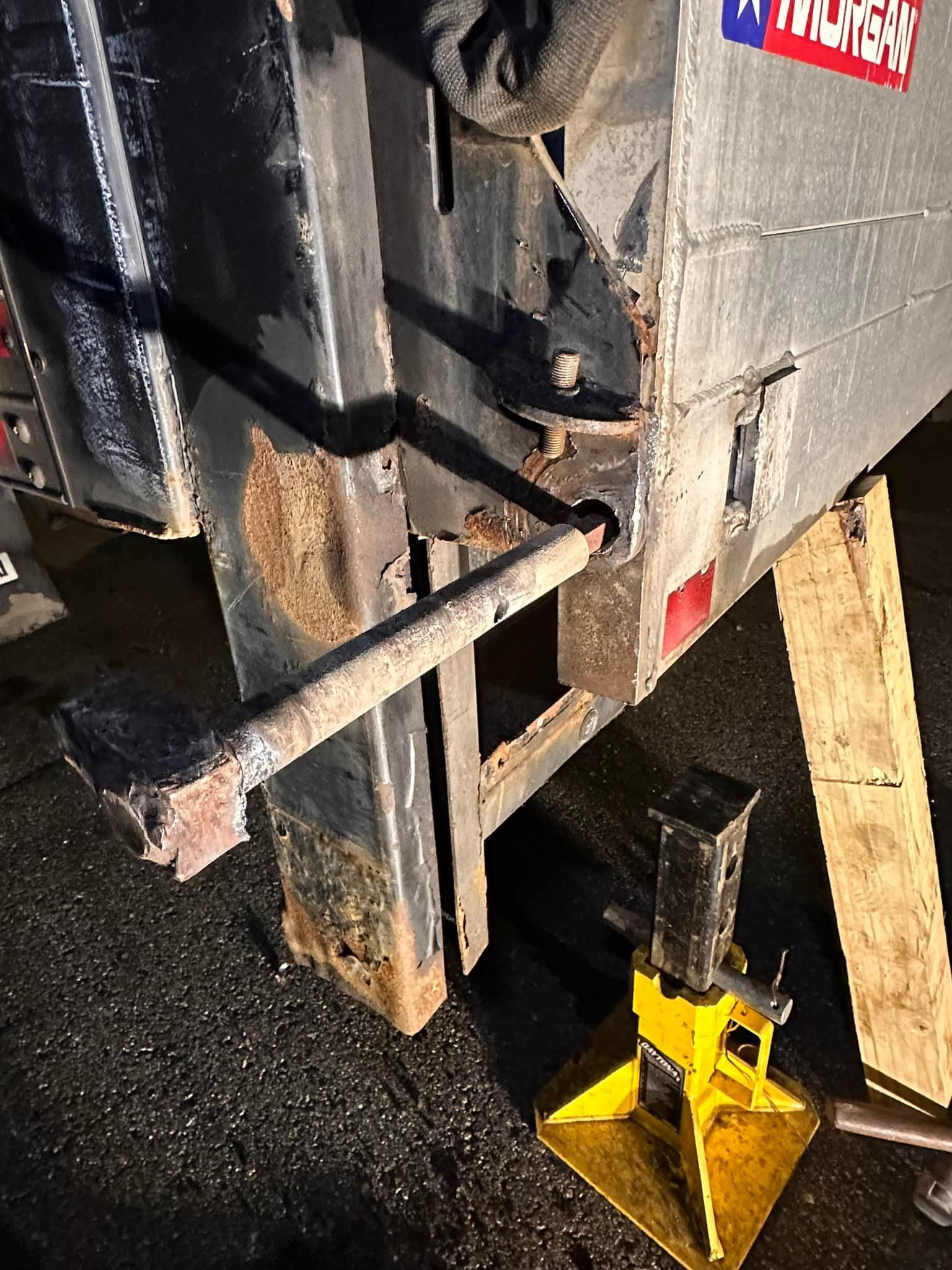 Damaged truck trailer supported by a jack. Rusty metal frame and loading ramp.
