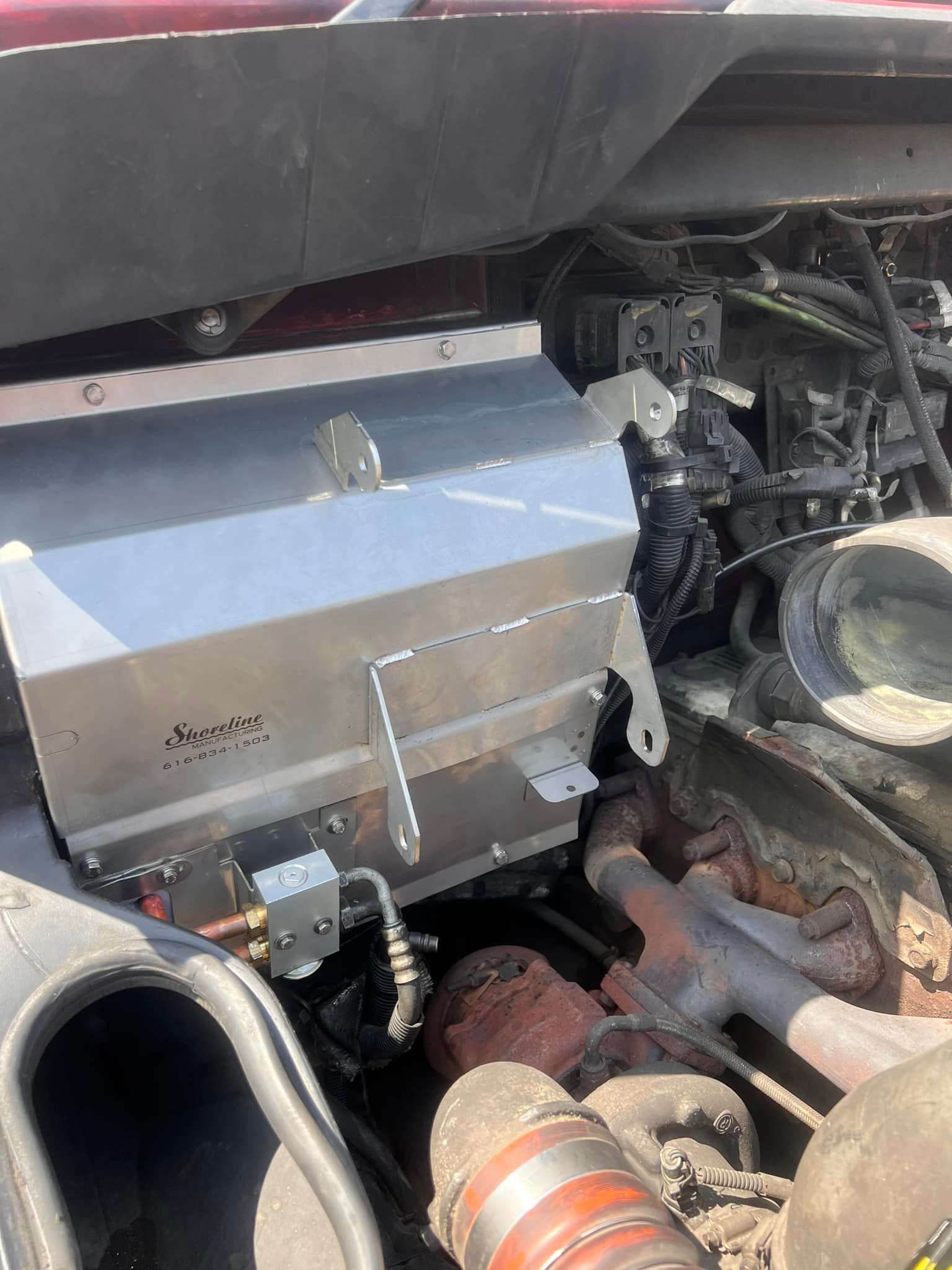 Close-up view of a truck engine with a silver metal box-like component installed, various hoses, and engine parts.