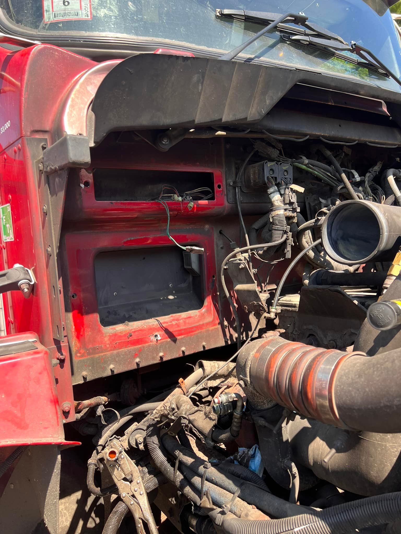 Red semi-truck engine compartment with exposed wiring and components.