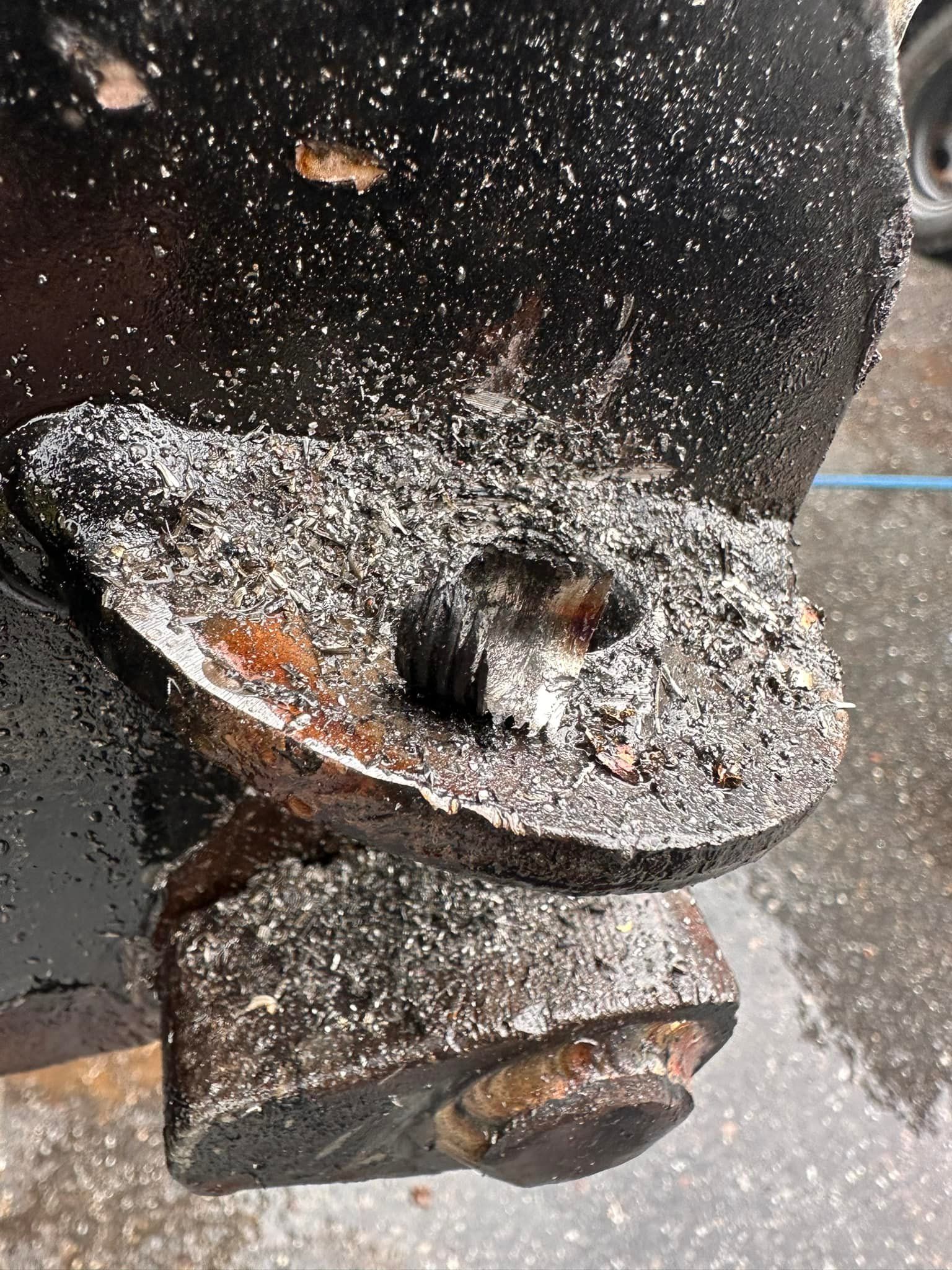 Close-up of a black metal component, likely automotive. Covered in white debris, possibly rust or corrosion.