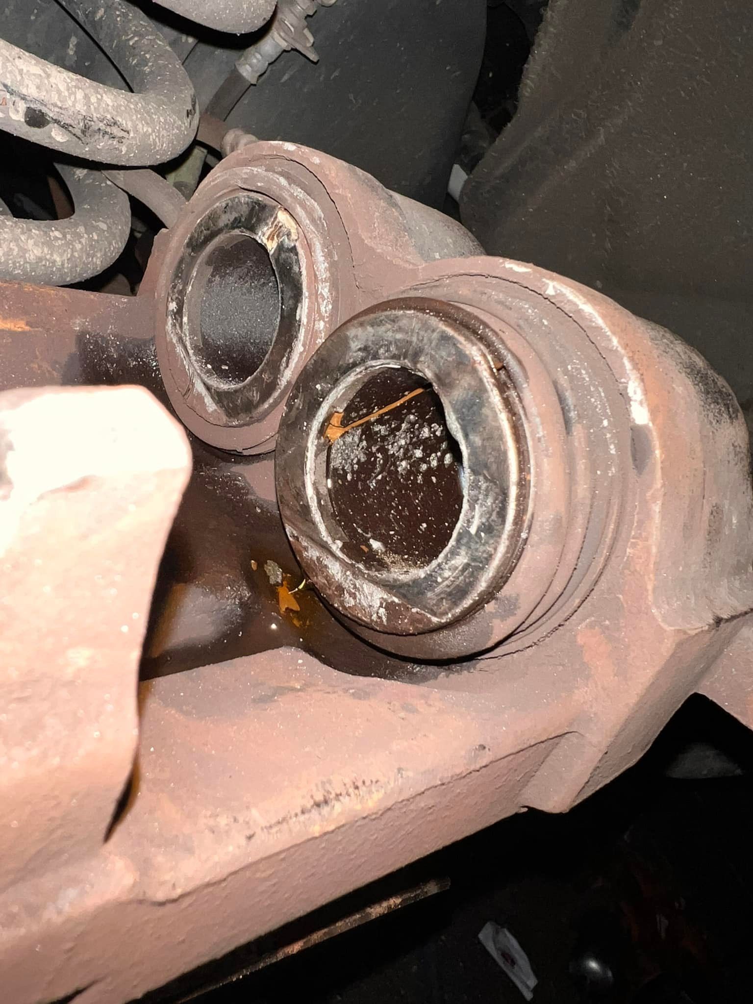 Close-up of a rusty car caliper with exposed cylinders and visible fluid.