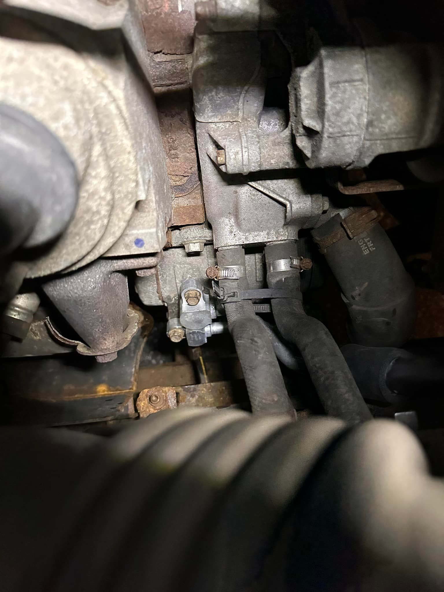 Engine component with various hoses, rust, and metal parts.