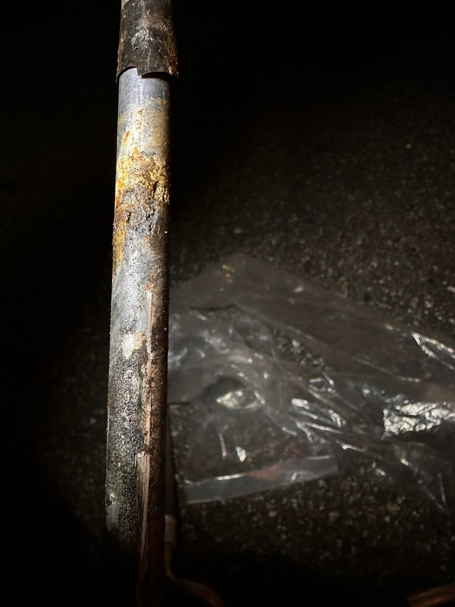 Rusty metal pipe with yellow corrosion, black background, plastic sheet.