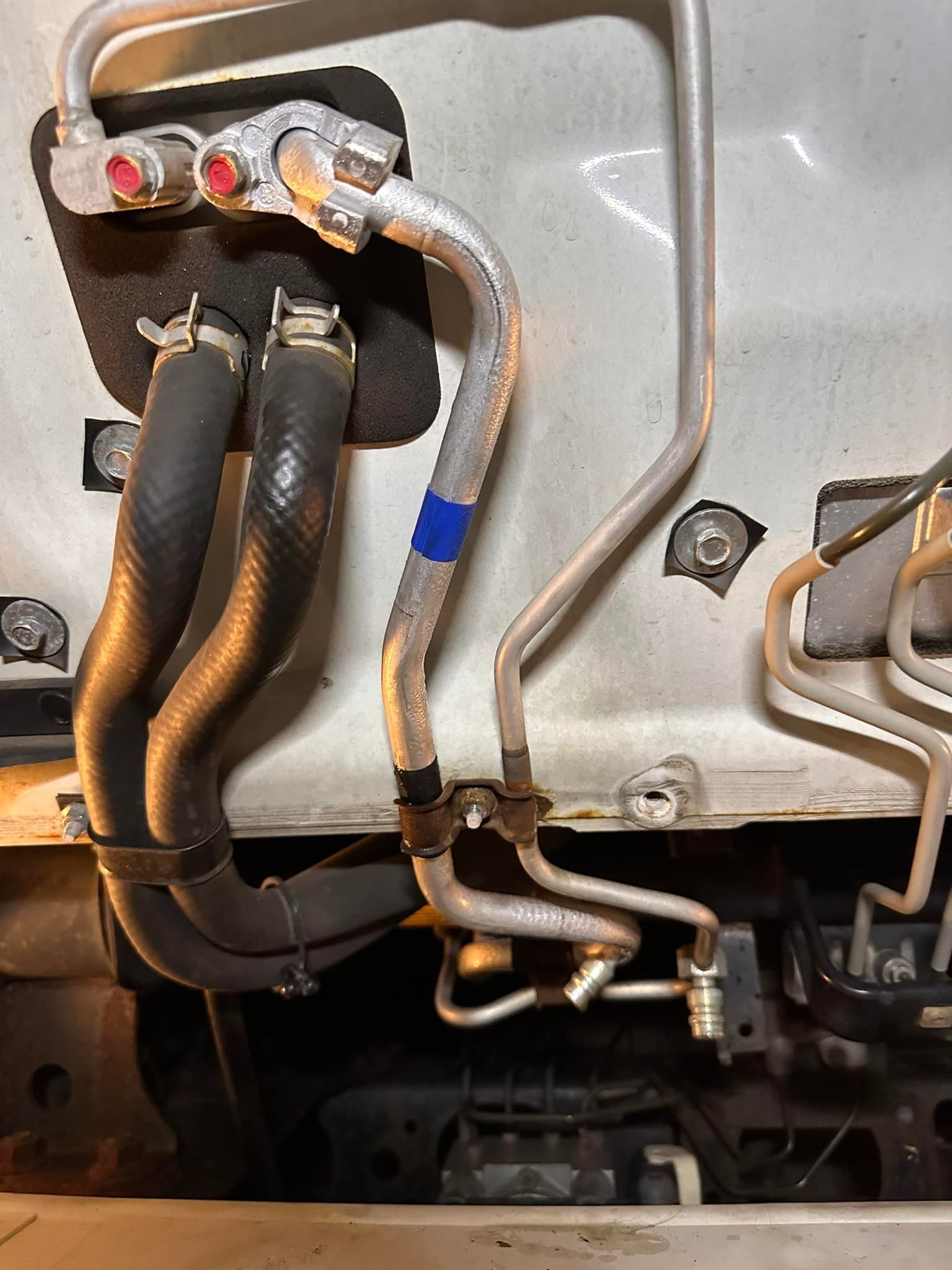 Car AC unit components; black hoses and metal tubes attached to a white body panel.