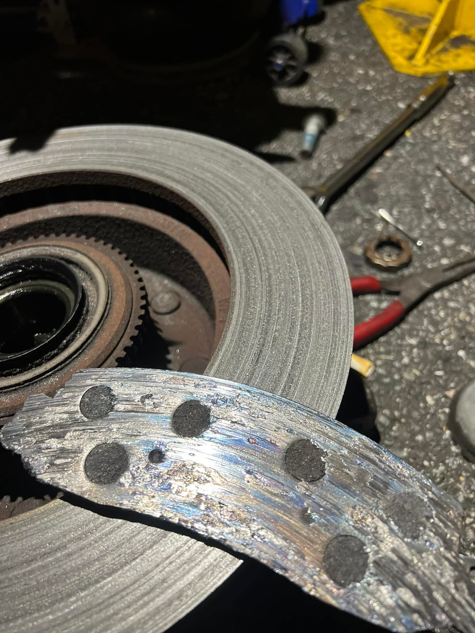 Damaged brake pad next to a brake rotor in a workshop. The pad is worn down with exposed metal.