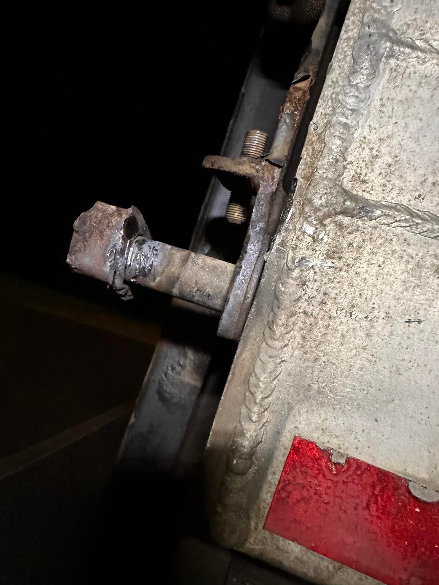 Close-up of a damaged metal latch welded to a panel, likely part of a vehicle. Rust and wear are visible.