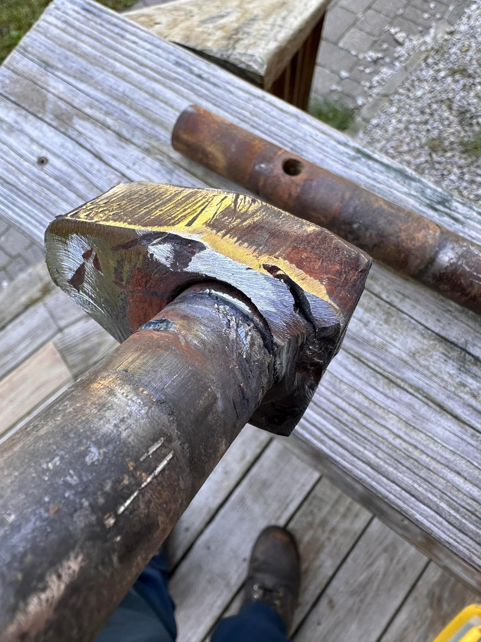 Rusty metal rod with a square head, set on a wooden surface with another rod in the background.