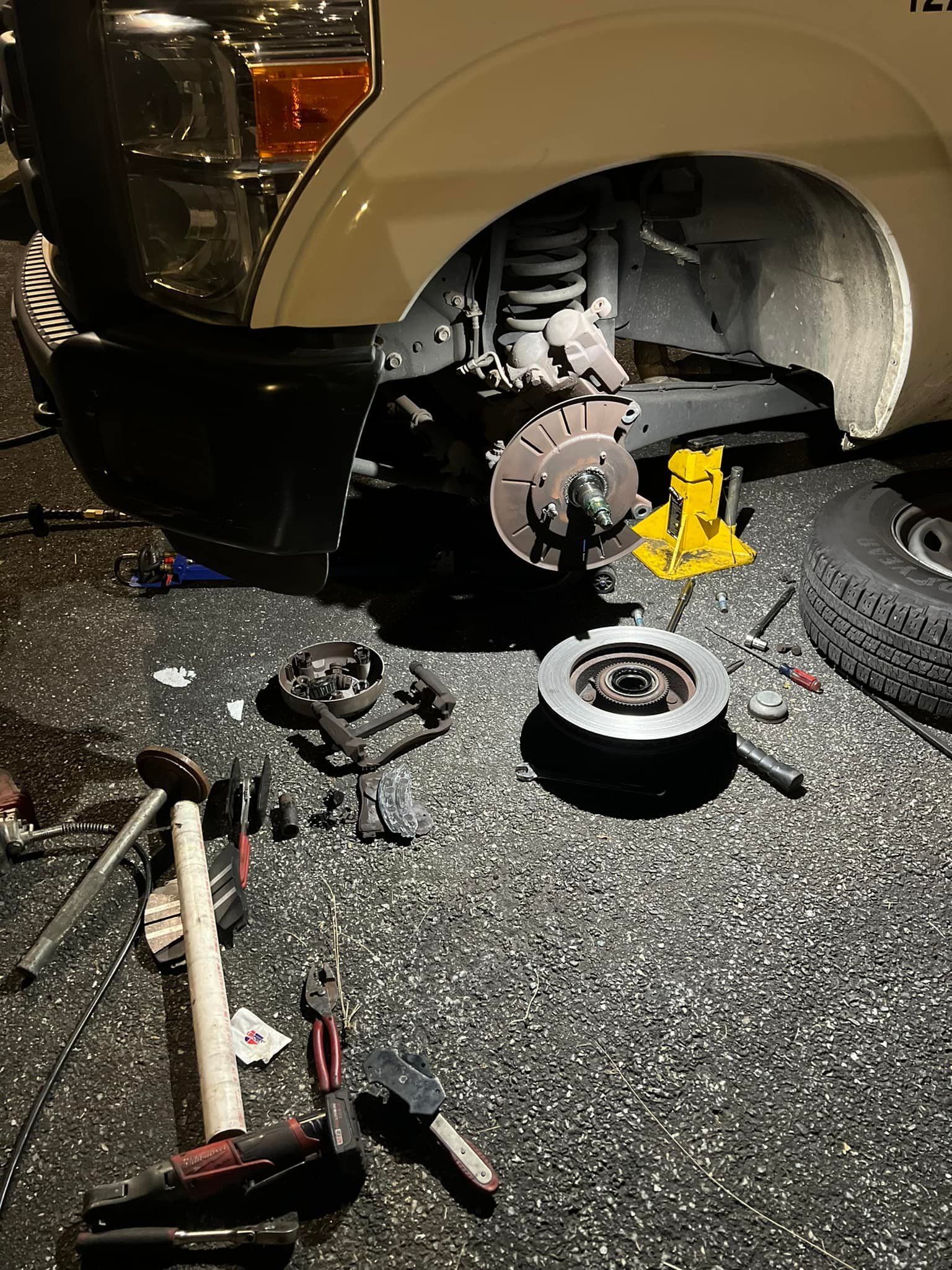 Car wheel removed; brake rotor replacement in progress; tools scattered on ground near jack.