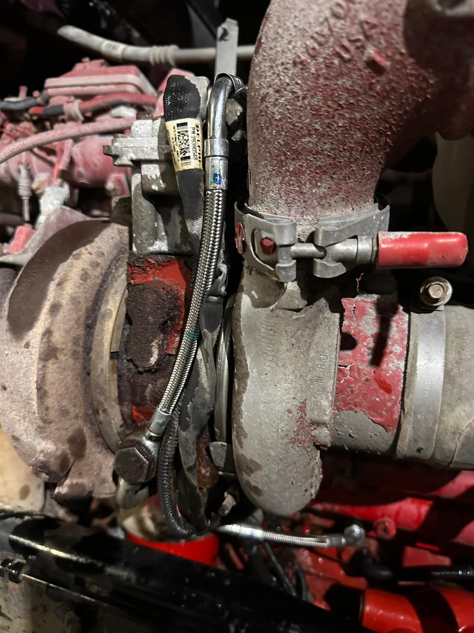 Close-up of a truck engine's turbocharger.  Exhaust manifold and oil lines are visible with a red, dusty appearance.