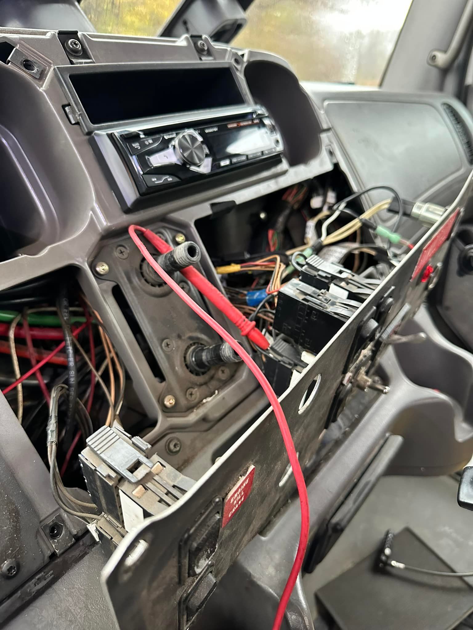 Dashboard of a vehicle with wires exposed, stereo installed, and components partially disassembled.