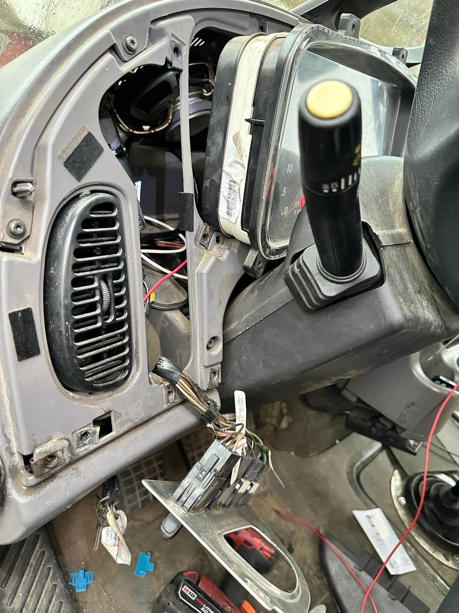Dashboard interior with removed panels, exposed wires, gearshift, and air vent.
