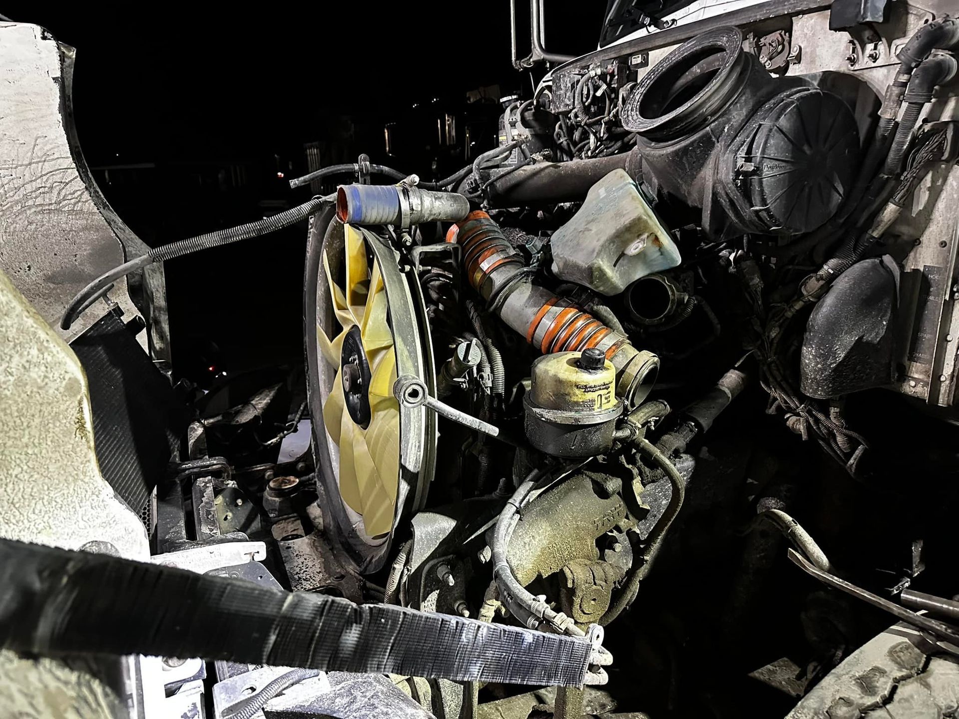 Engine compartment of a burned truck, showing damaged components and dark setting.