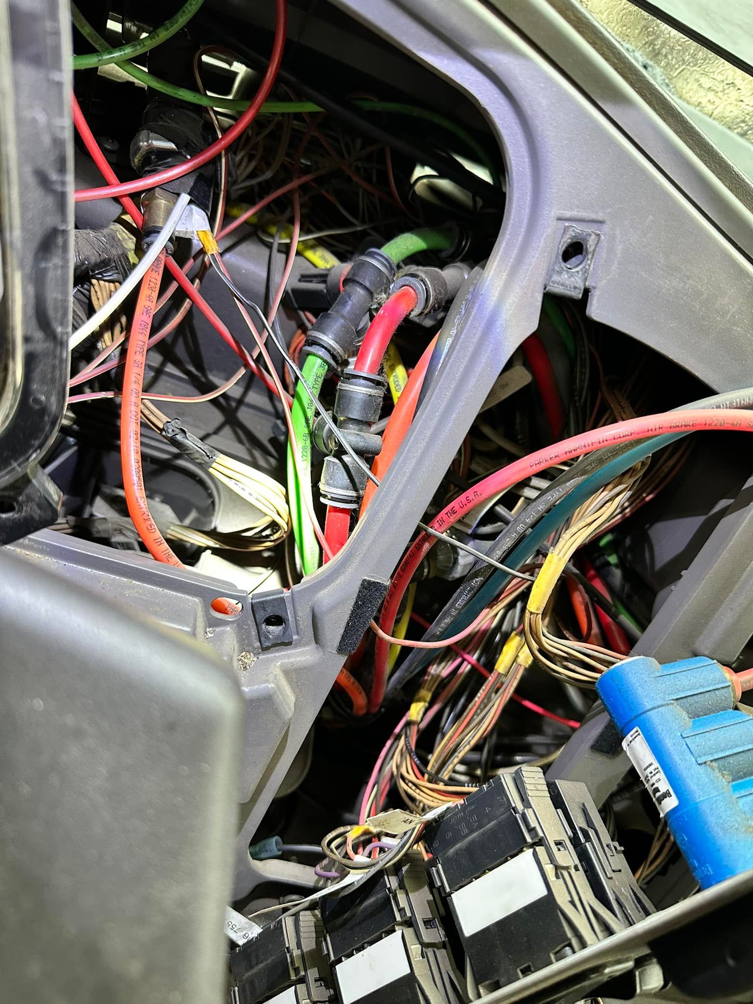 Bundle of colorful wires and cables inside a vehicle's dashboard, with black connectors and a blue electronic device visible.