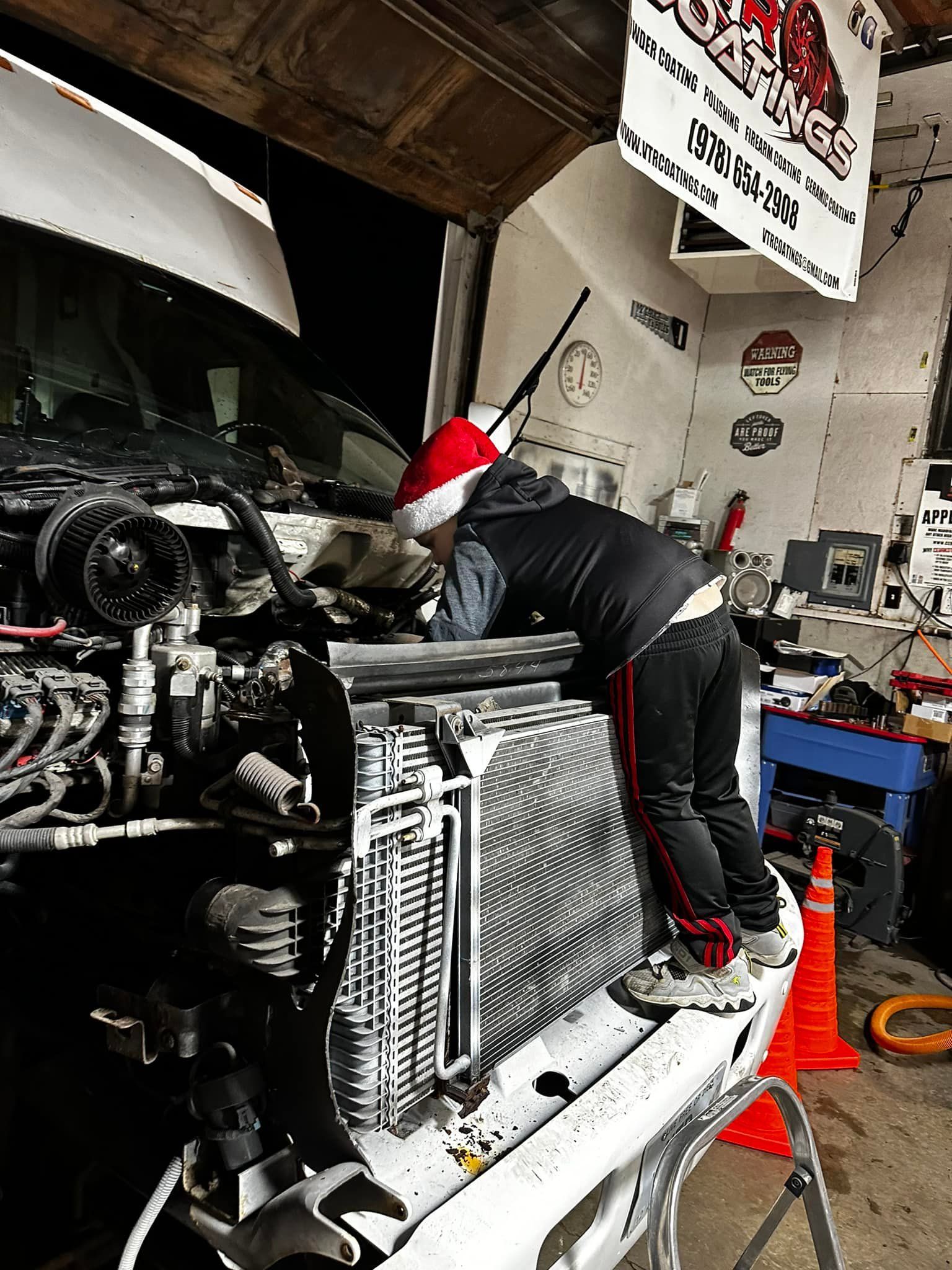 Person in Santa hat working on a vehicle engine in a garage.