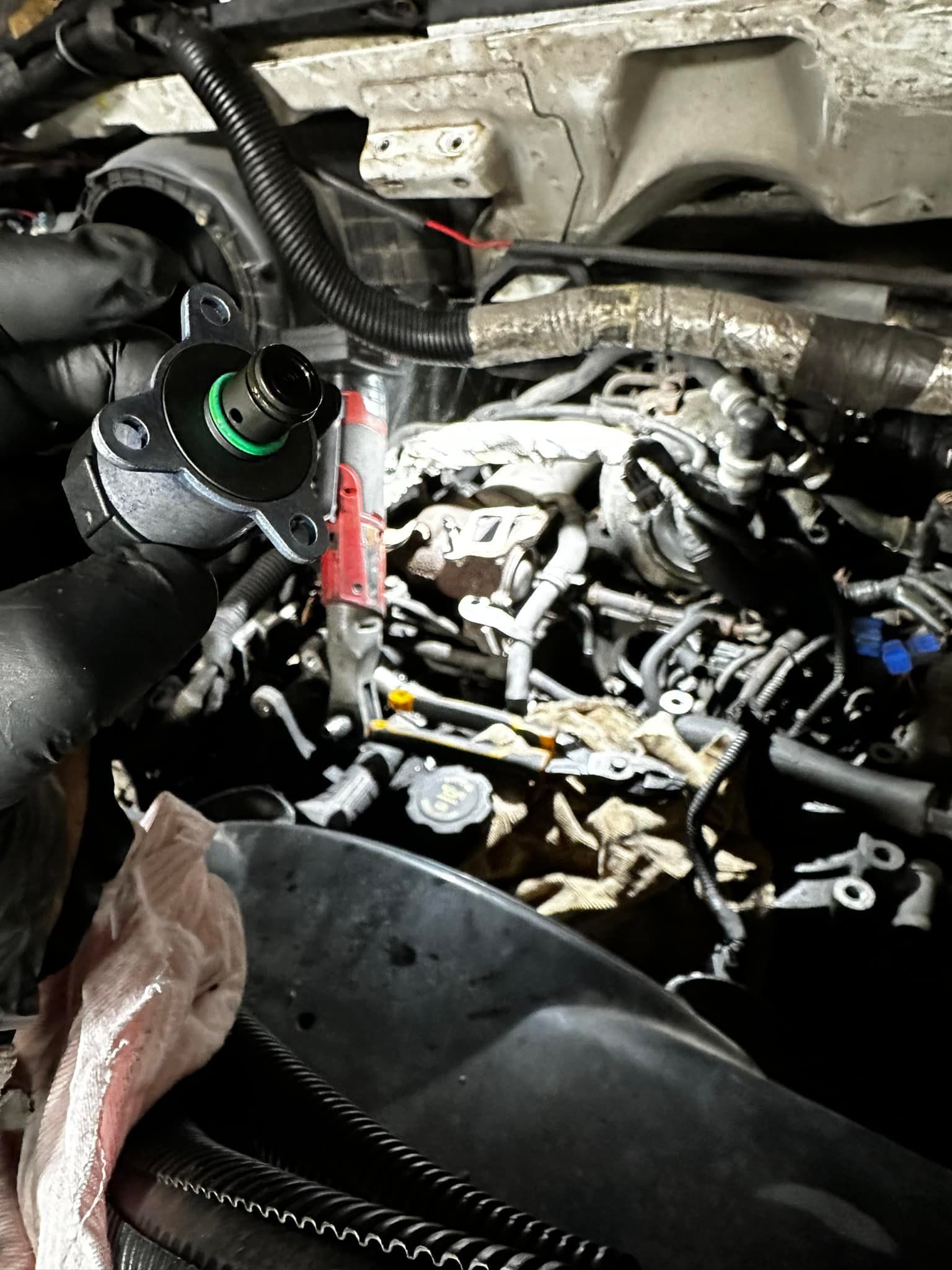 Engine bay with mechanical tools and components. Black hose, wiring, and red tool present.