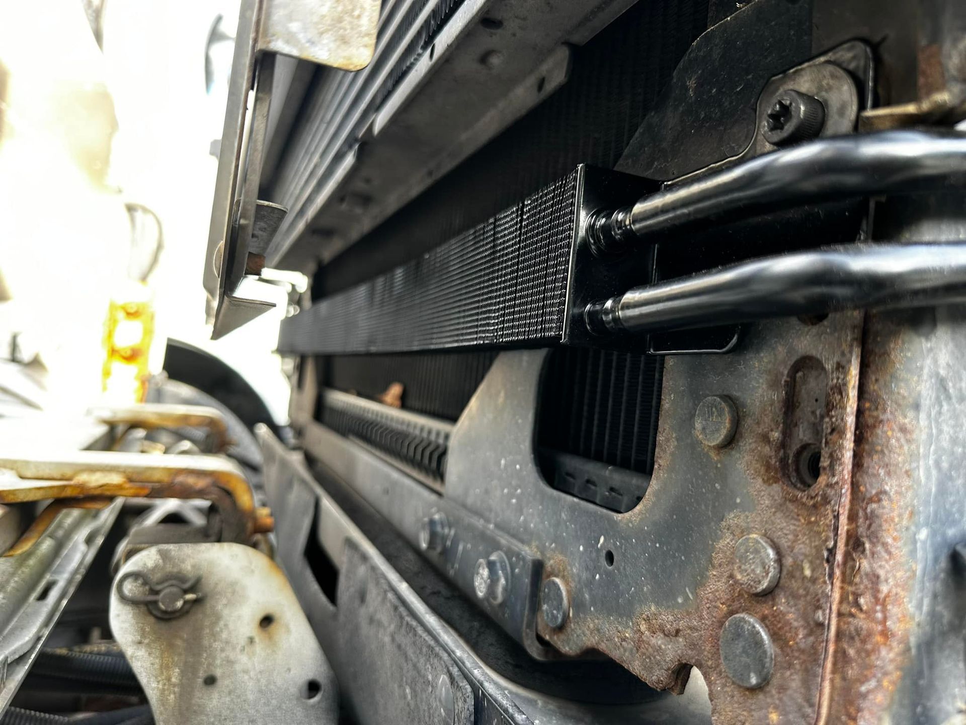 Car's radiator and oil cooler. Black tubes connect to the cooler, mounted to a rusty metal frame.