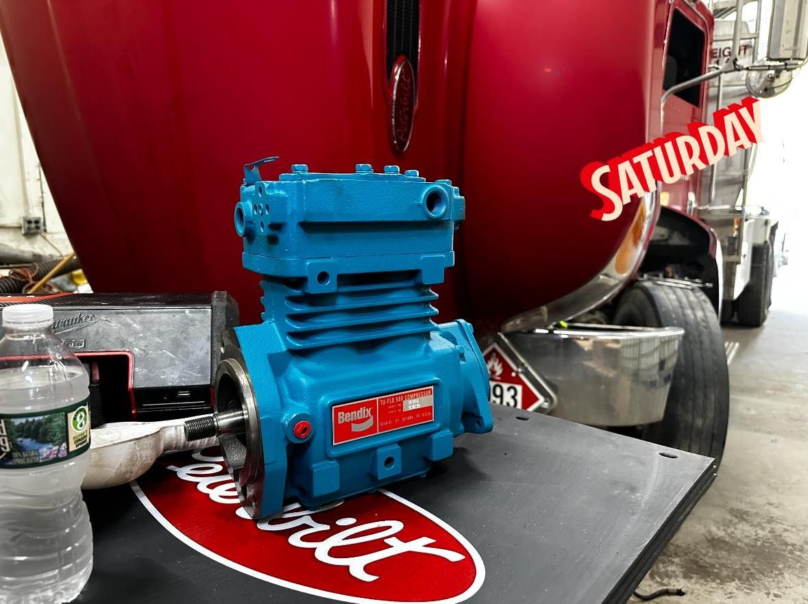 Blue air compressor on a Peterbilt logo mat, in front of a red truck.
