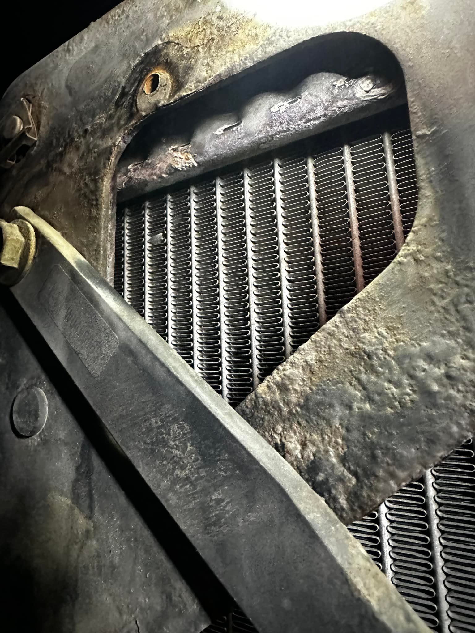 Close-up of a damaged radiator. The metal frame is rusty, with the cooling fins visible inside.