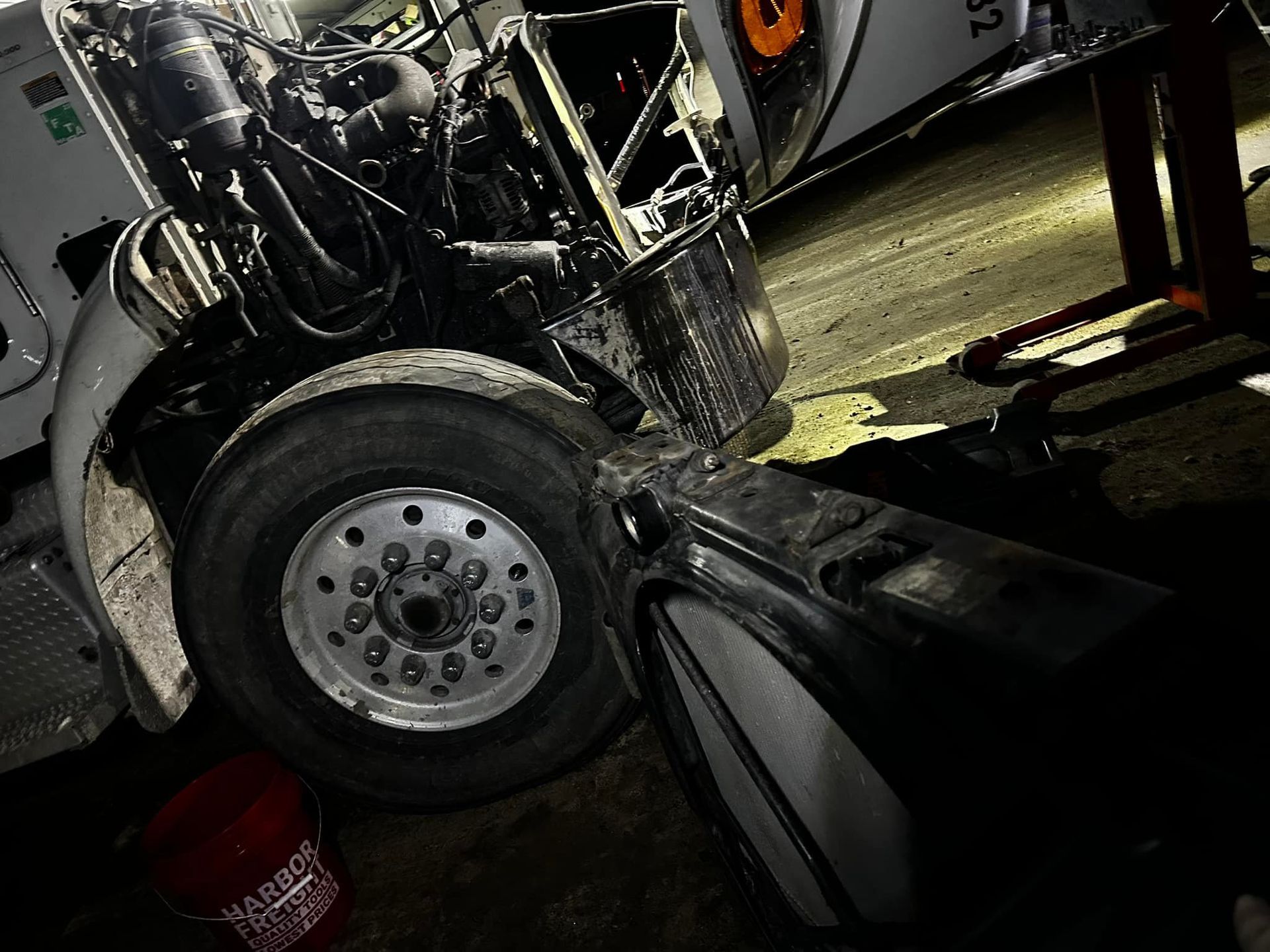 Semi-truck with open hood; front tire visible.  Black engine, silver wheel, white fender.  Dark setting.