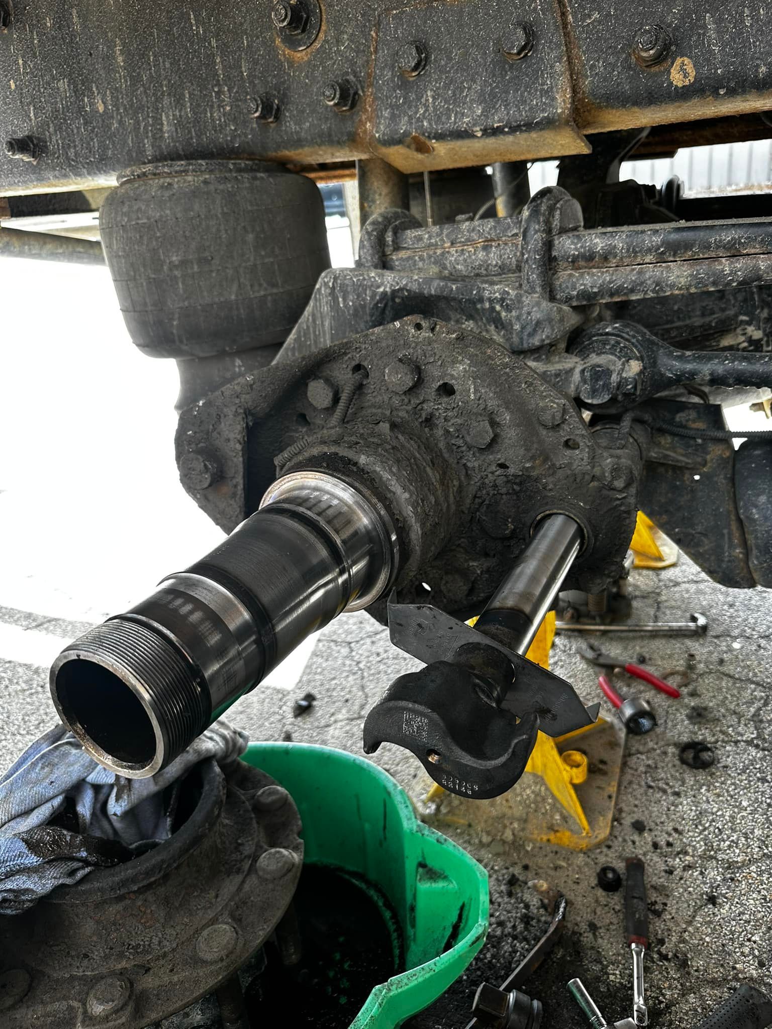 Truck axle being disassembled, showing a greasy spindle and components in a repair setting.