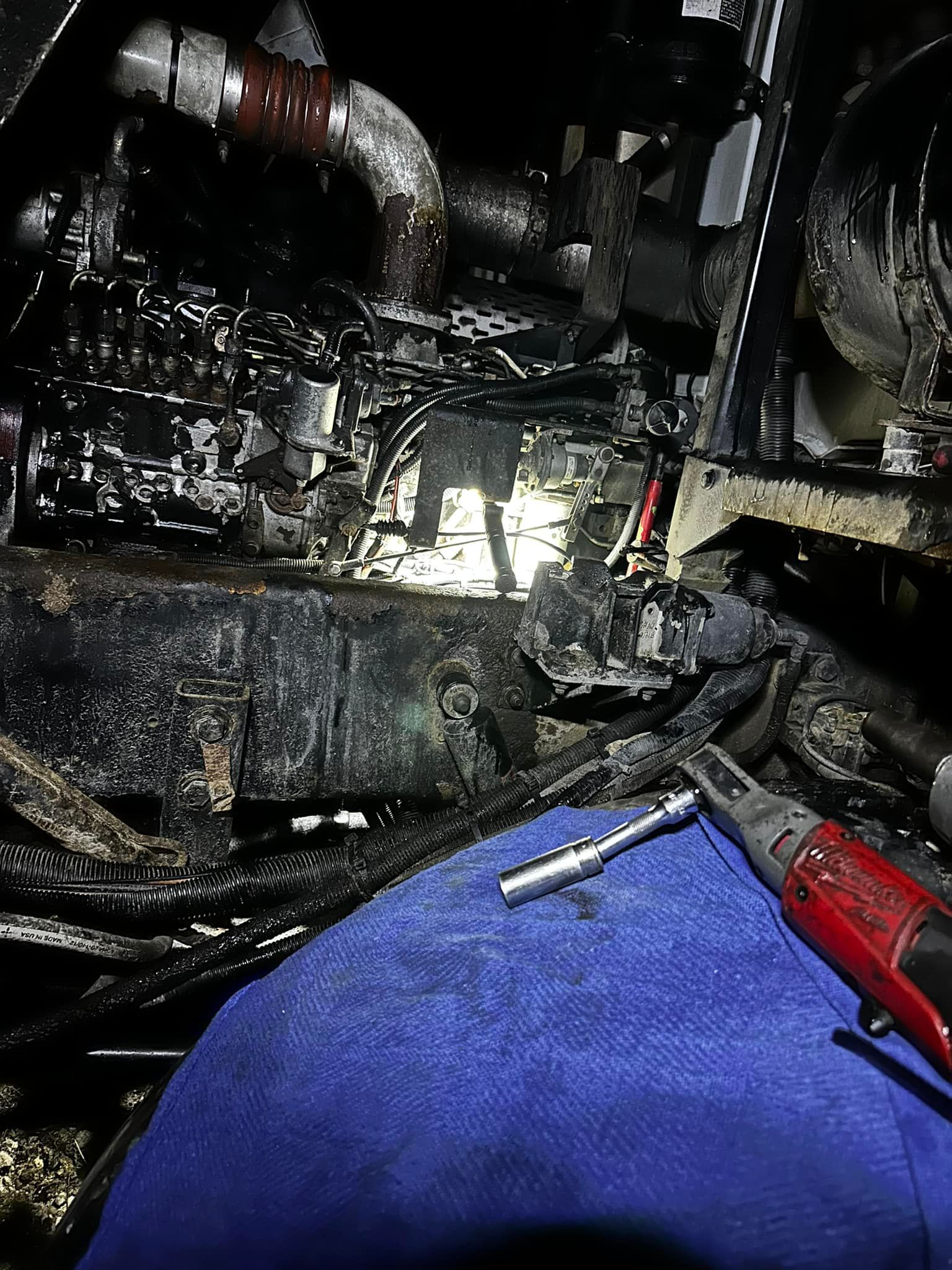 Inside engine compartment, mechanic in blue overalls, tools in hand, working on blackened components.