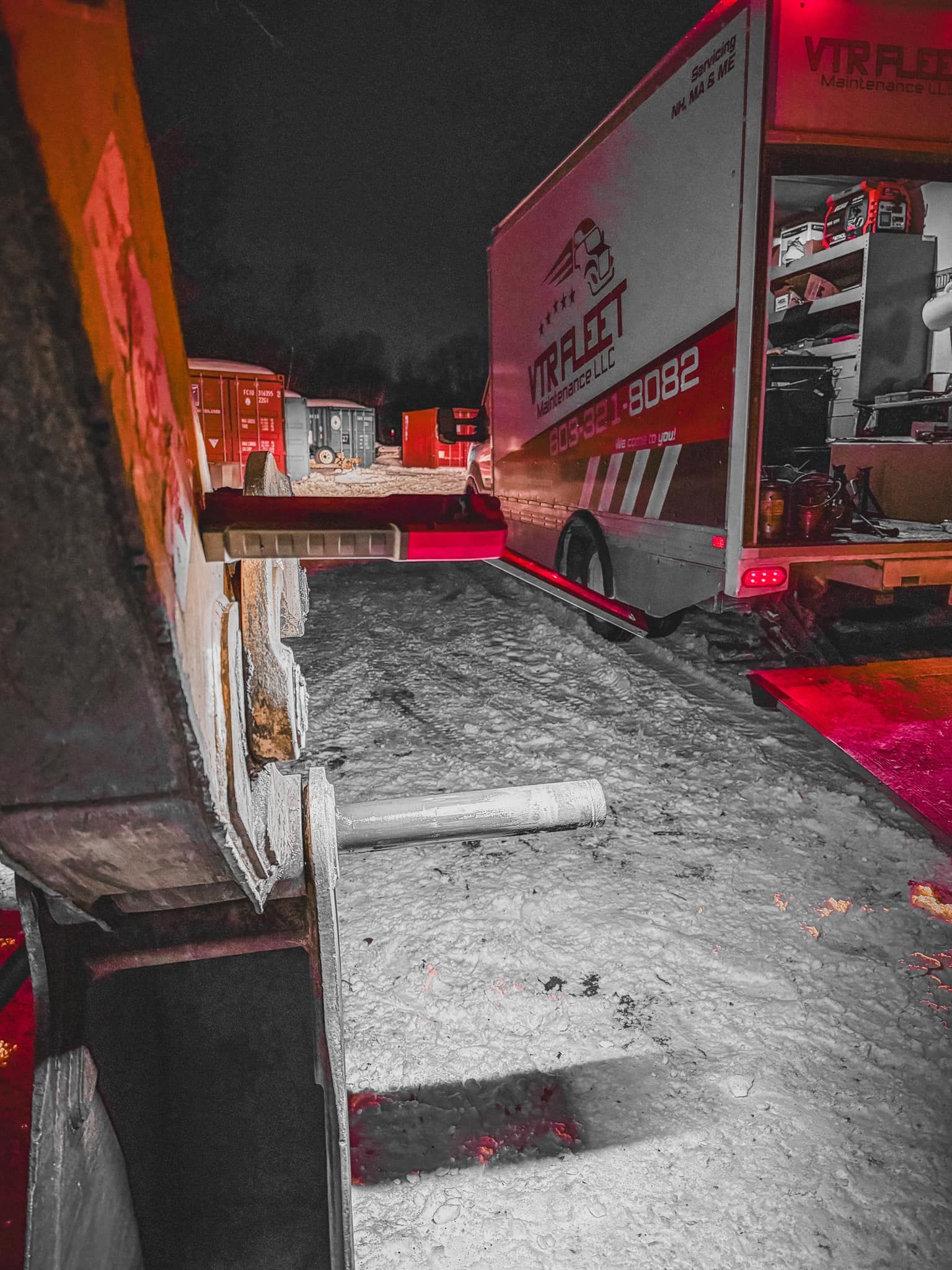 A ramp extends to a truck at night. The truck has an open cargo bay with equipment. Red lights are visible.