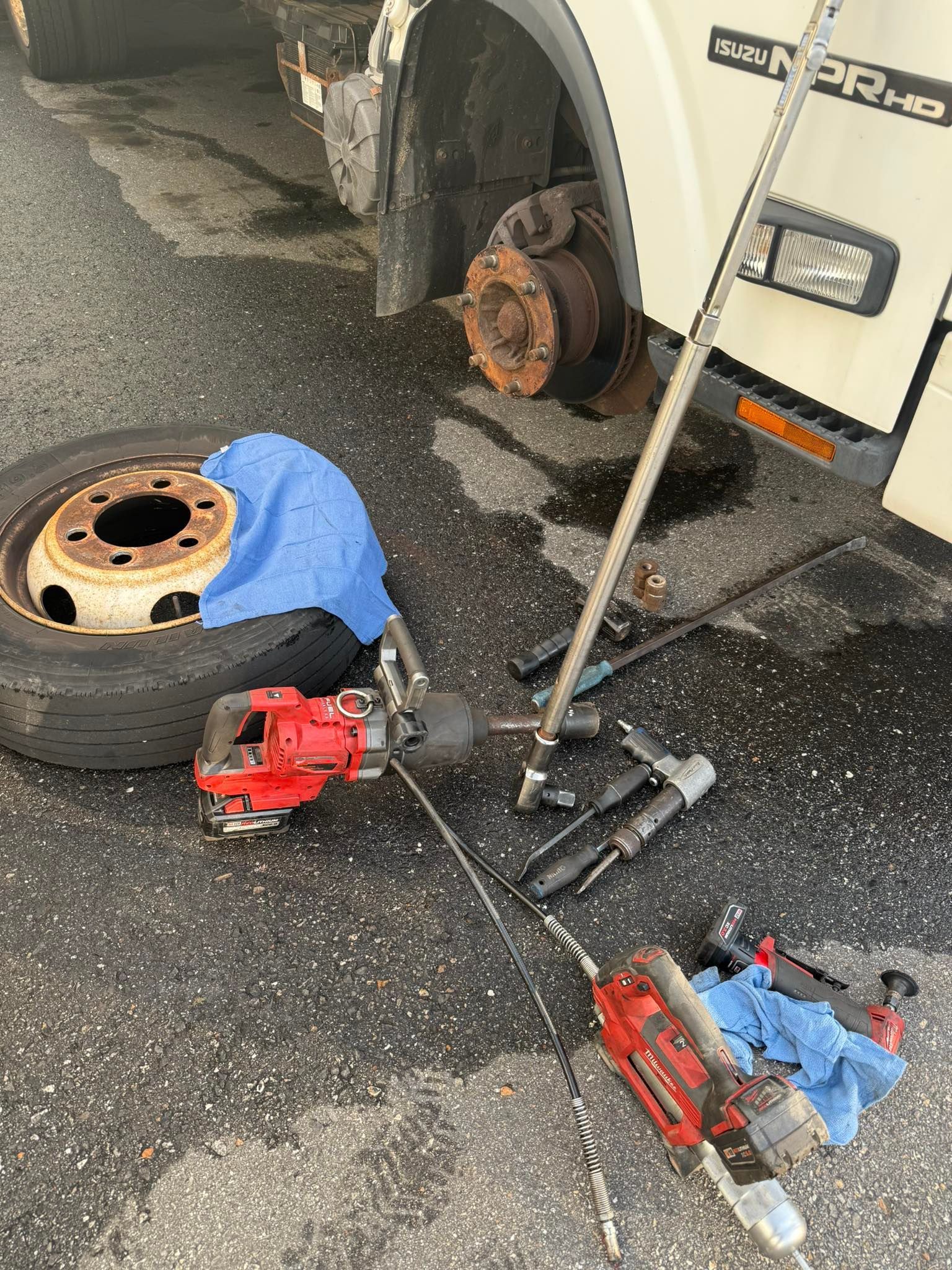 A truck tire removed, tools scattered on asphalt; rusty brake rotor visible.