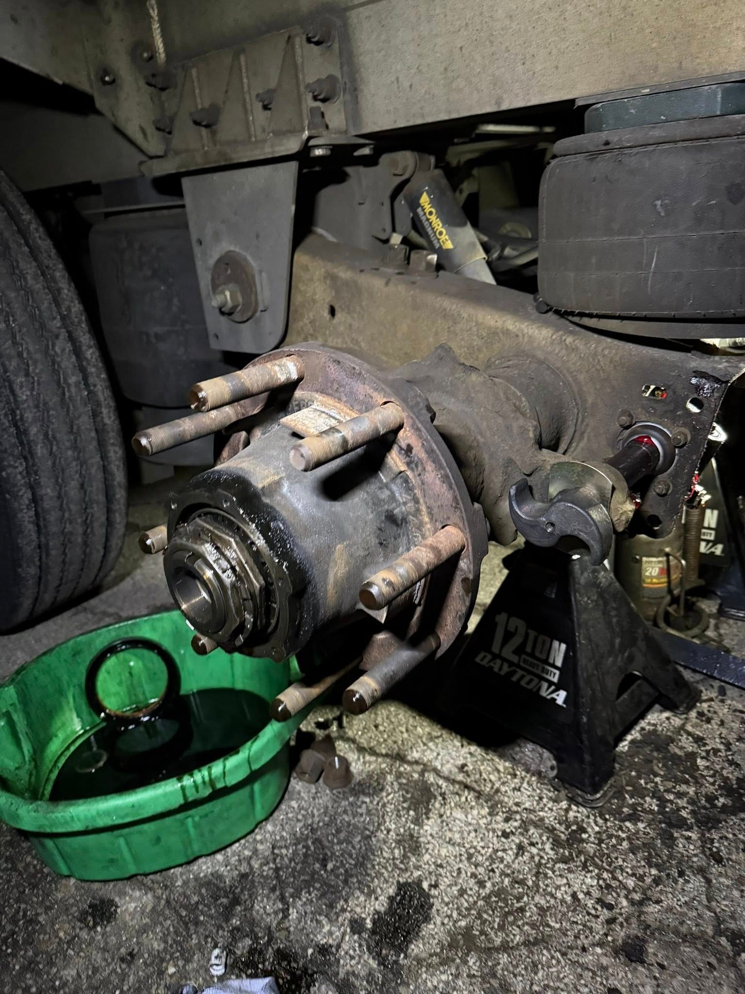 Truck's axle assembly being worked on with oil drain pan, jack stand, and hub exposed.